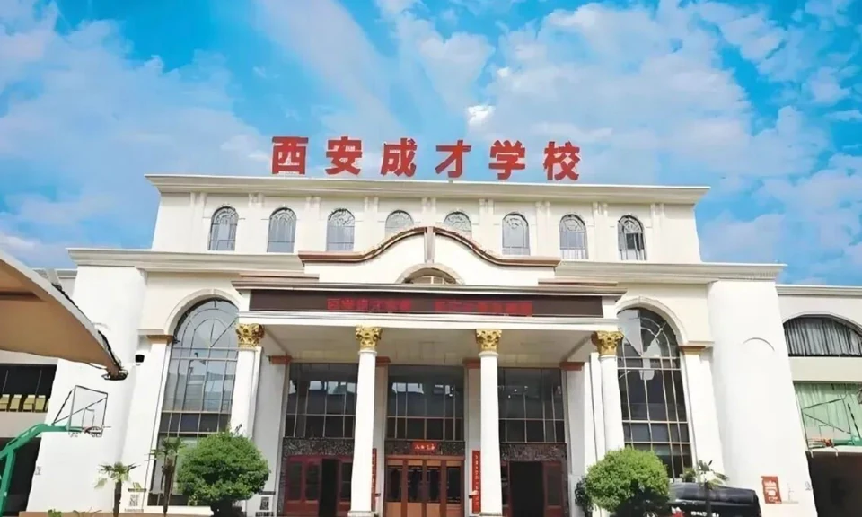 西安成才学校教学楼外景，白色多层建筑，顶部有红色「西安成才学校」校名标识，正门为柱廊式入口