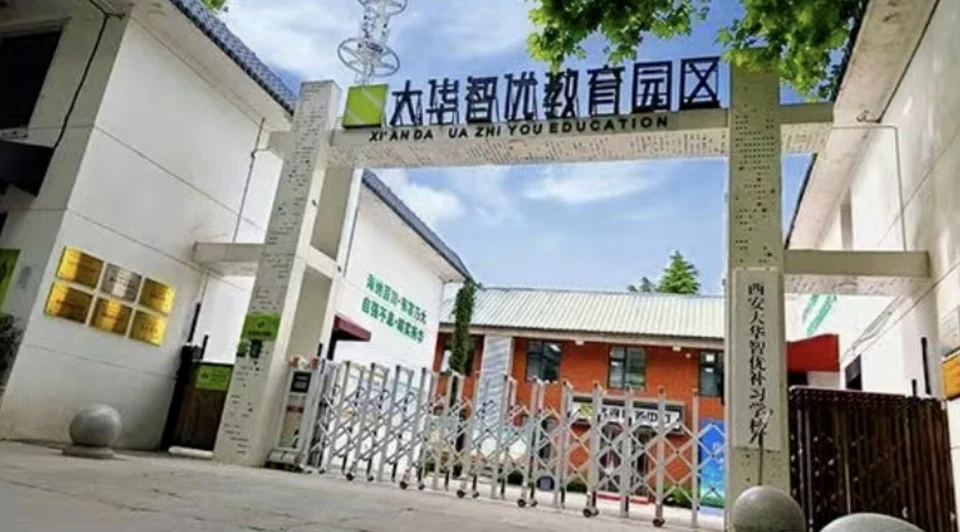 西安大华智优教育园区入口，门头写有大华智优教育园区字样，下方英文标识 XI AN DA HUA ZHI YOU EDUCATION，可见白色围墙、伸缩门与彩色宣传栏