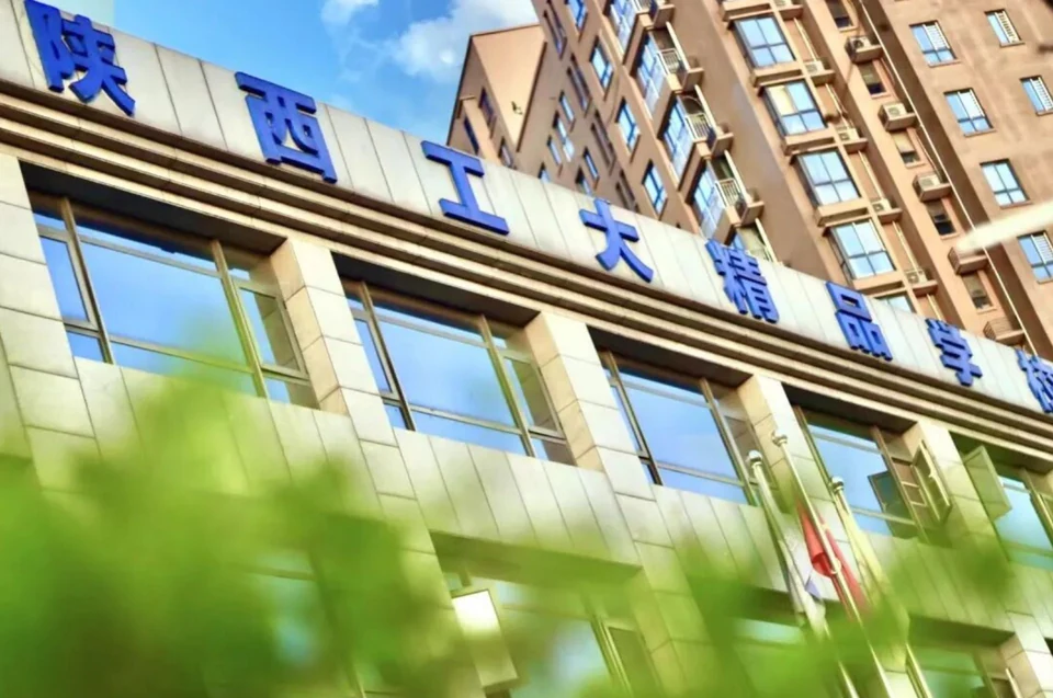 陕西工大精品学校教学楼外景，蓝色校名大字嵌在浅色石材立面上，楼前有绿树与旗杆