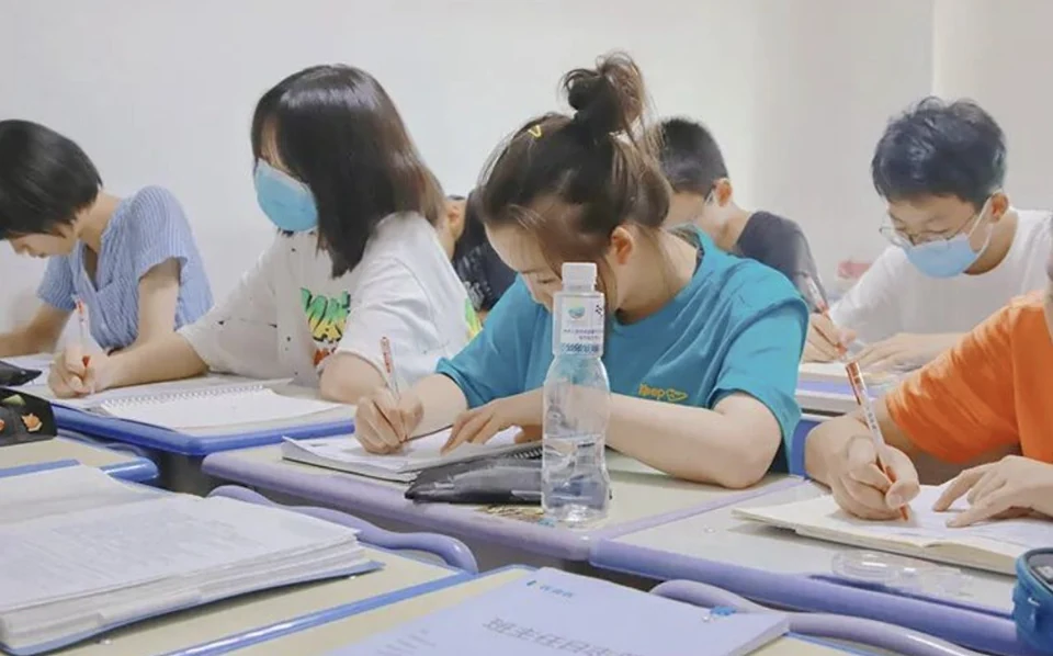 高考全日制补习课堂实景，学生分组落座在教室内低头做题，桌面摆放讲义与错题整理本